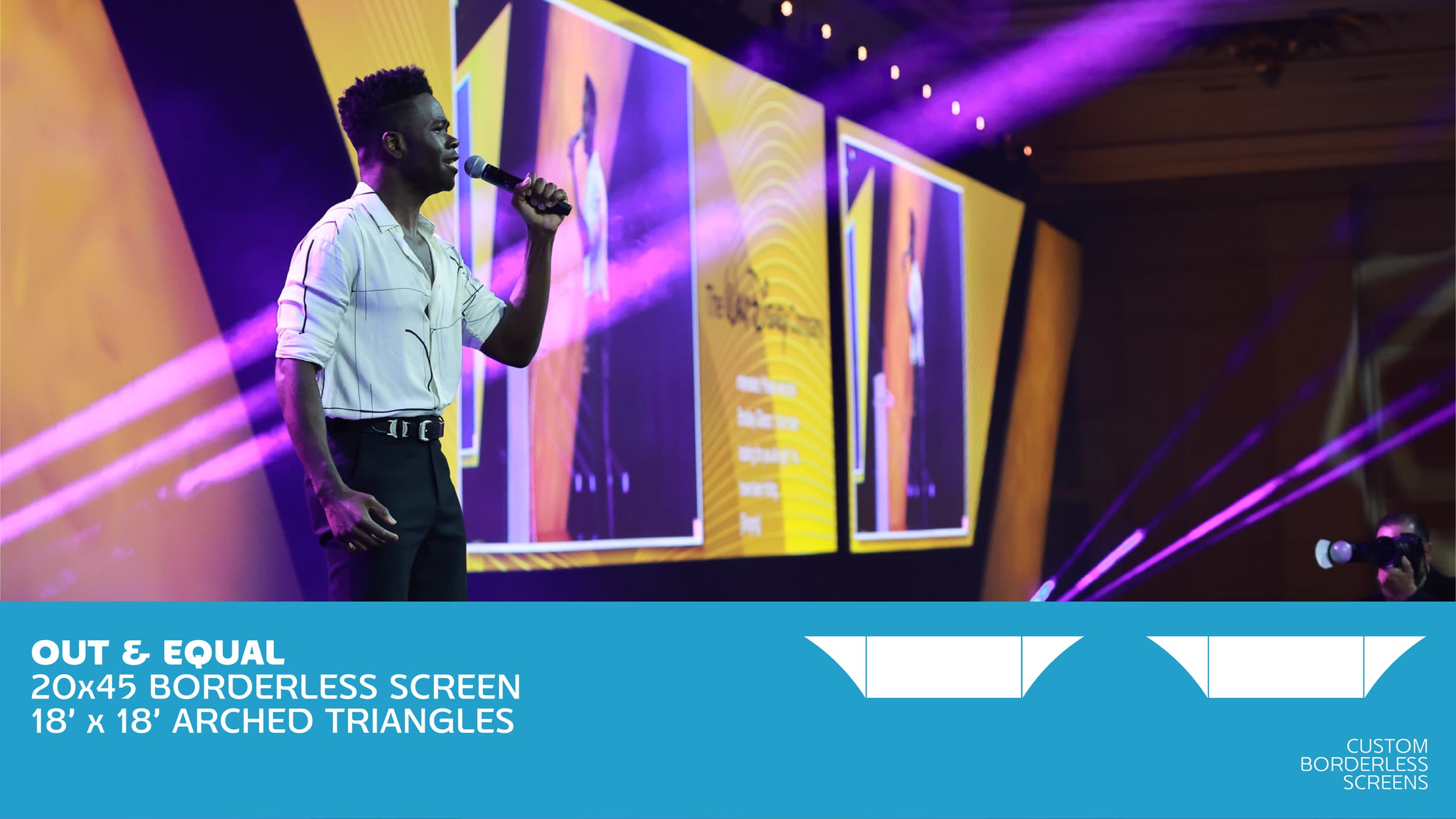 A man holding a microphone on stage with large yellow screens and purple lighting in the background
