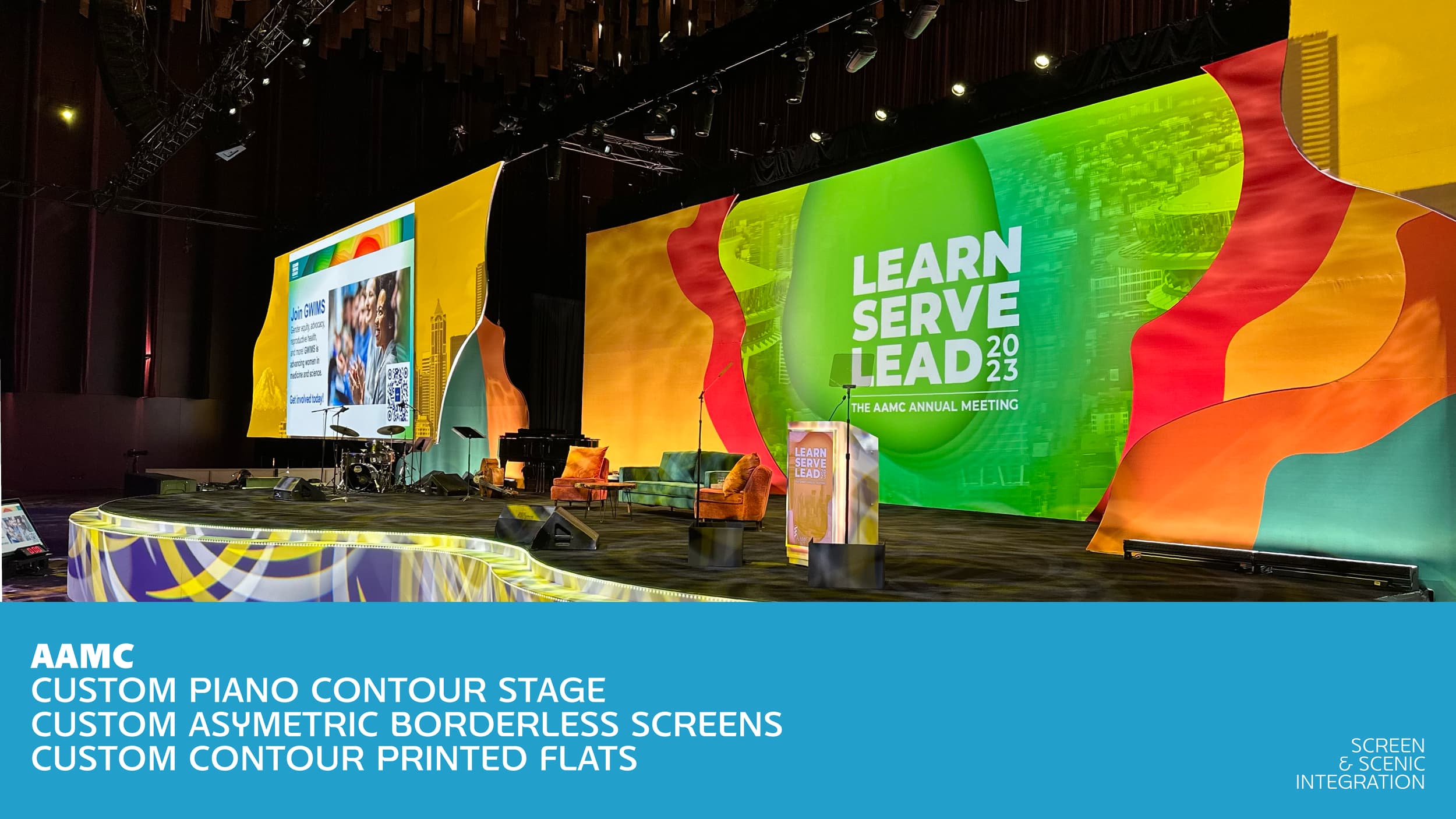A large stage with a colorful, abstract backdrop featuring a digital screen displaying event information, music instruments including drums and a grand piano, and multiple chairs for speakers or performers at the 2023 AAMC annual meeting with a theme