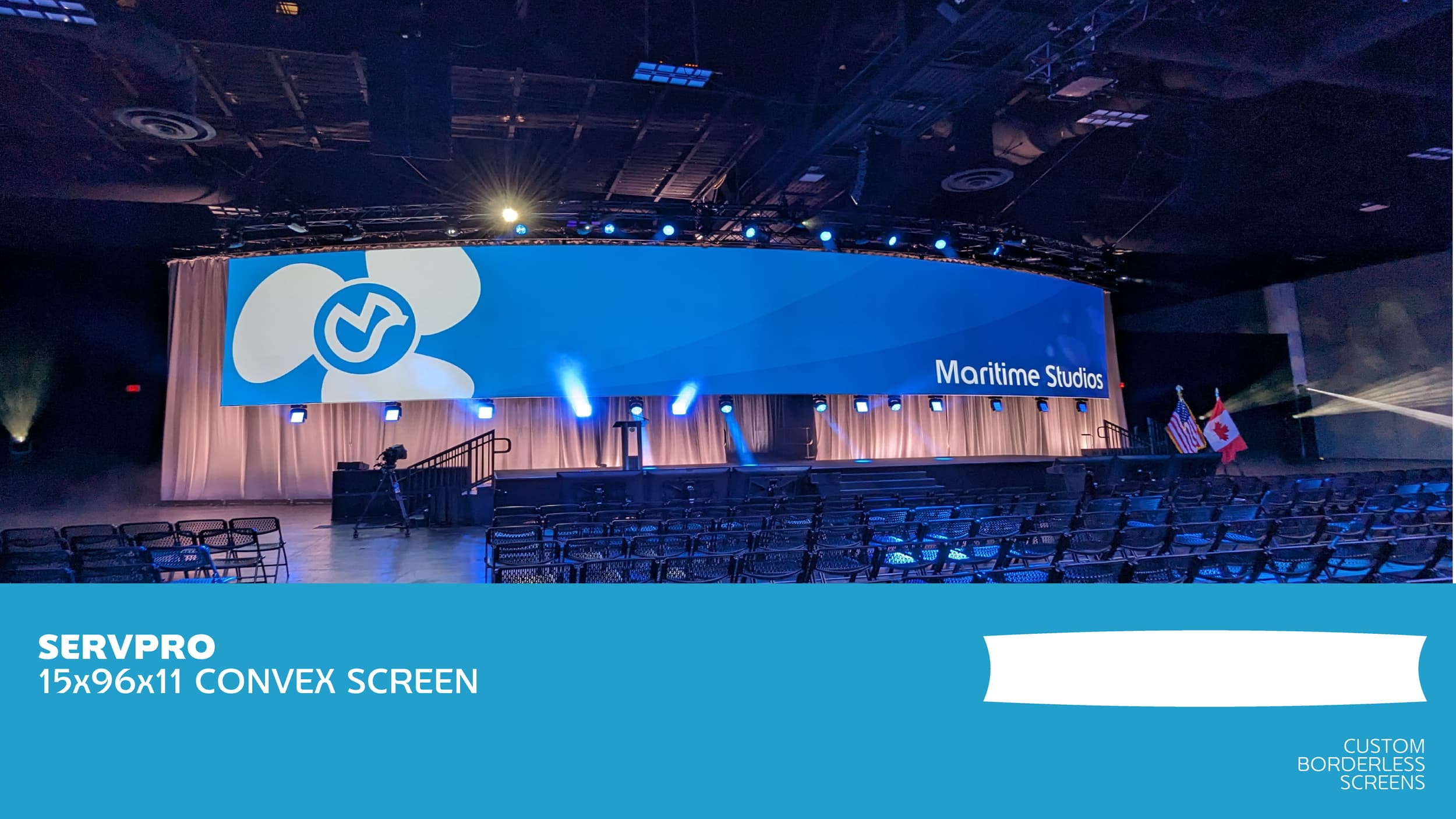 Large conference stage with a wide curved blue screen displaying the words 'Maritime Studios' and a logo. Auditorium seating in front, with national flags of the United States and Canada to the right of the stage. Stage lighting and equipment visible