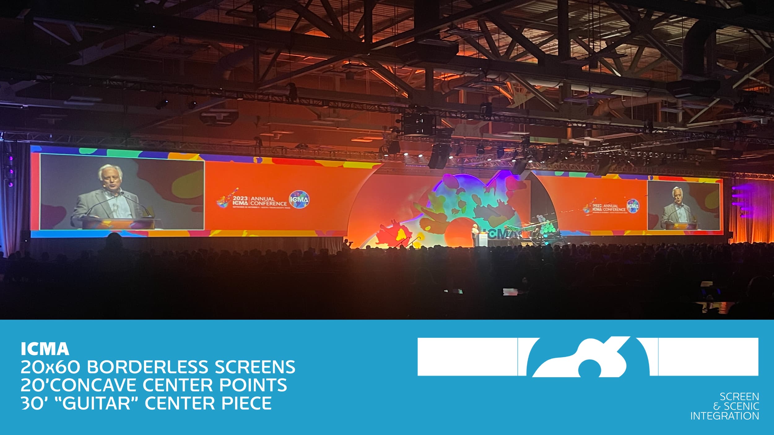 A large conference room filled with people attending the 2023 ICMA Annual Conference. The stage features a lone speaker at a podium, with two large curved screens on either side displaying the speaker's image. The background has colorful and abstract